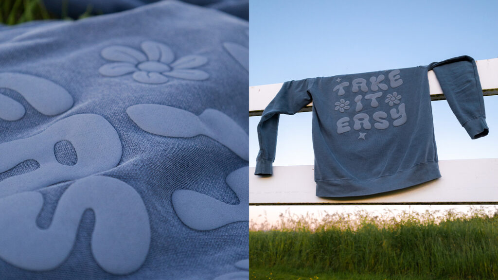 Blue fabric with white flower pattern on the left; a blue sweatshirt with 'Take It Easy' draped over a fence on the right, outdoors under a blue sky.