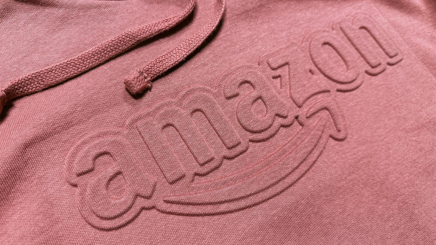 Close-up of pink hoodie fabric with an embossed wordmark running across it.