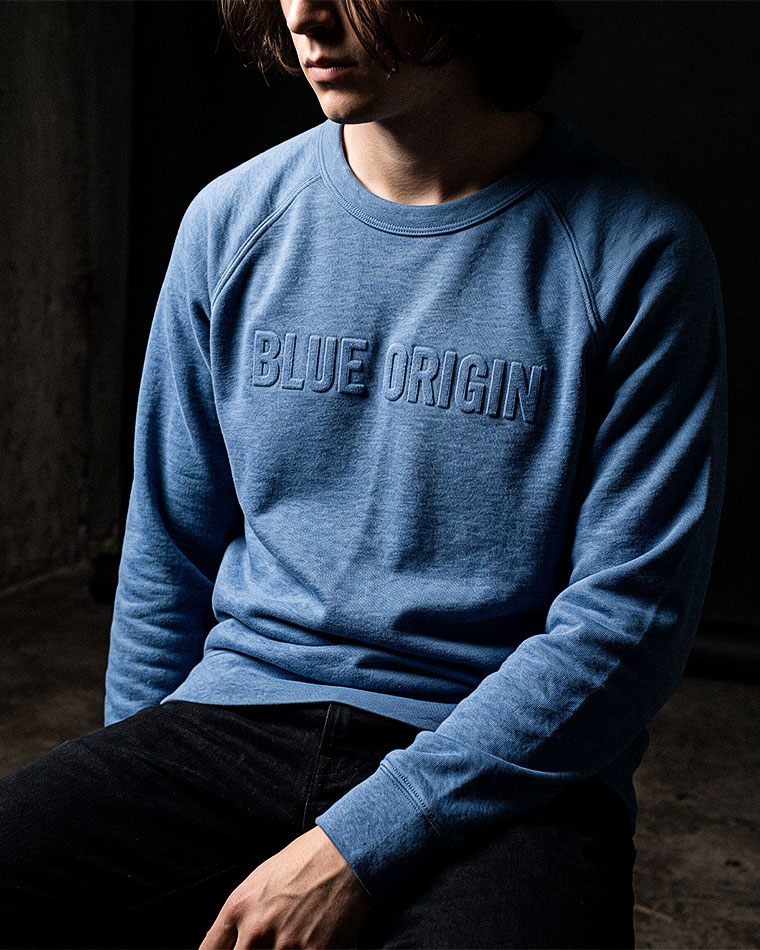 Person wearing a blue crewneck sweatshirt with 'BLUE ORIGIN' embossed on the chest.