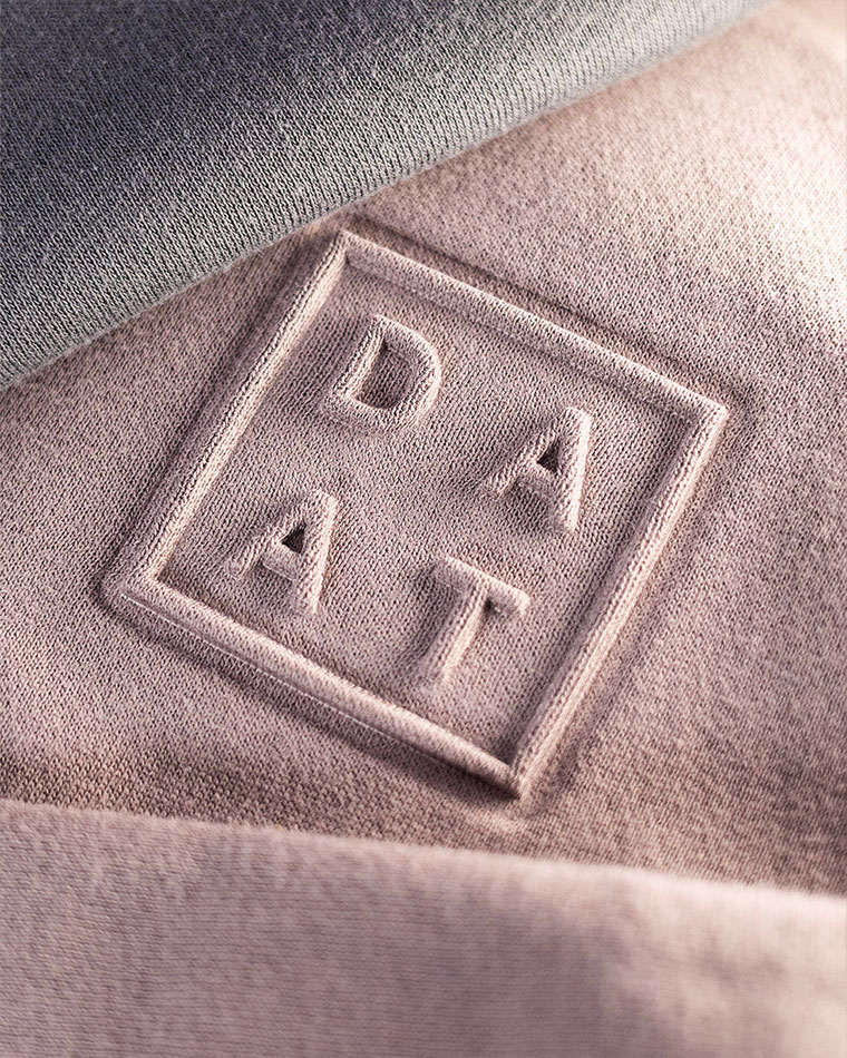 Close-up of pale pink fabric with an embroidered square patch containing the letters DAT.