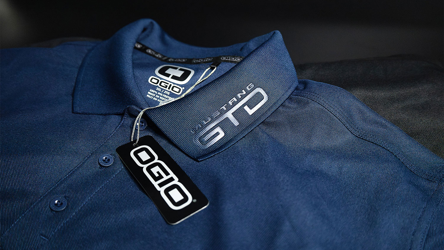 Close-up of a blue polo shirt collar with an OGIO tag and hanging label attached.
