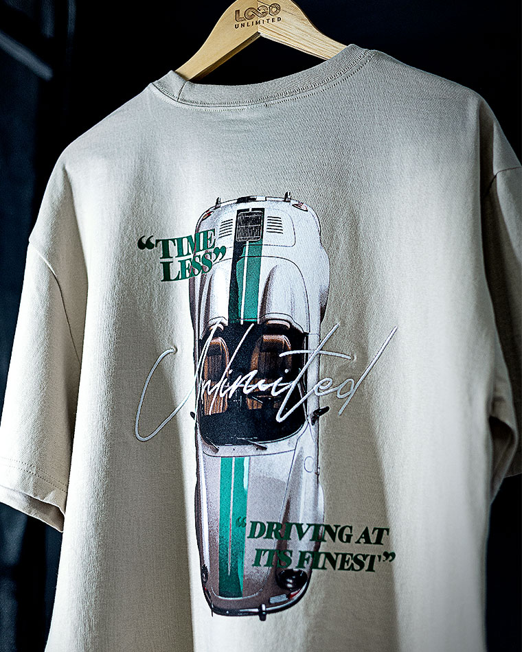 Beige T‑shirt on a wooden hanger showing a white sports car graphic with teal stripes and the caption 'DRIVING AT ITS FINEST'.