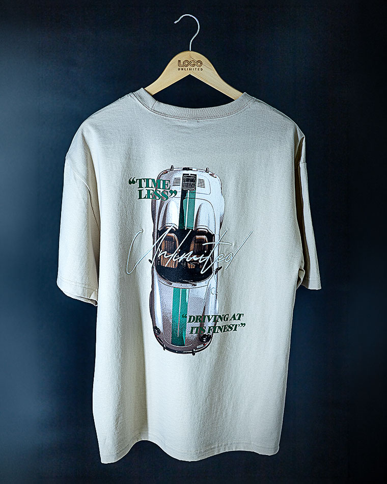 Beige t‑shirt on a wooden hanger against a dark wall, featuring a vintage car graphic with teal stripes and the words 'TIMELESS' and 'DRIVING AT ITS FINEST'.